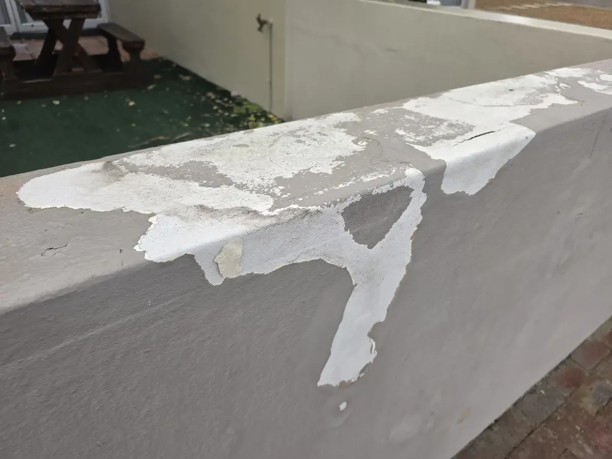 Extensive peeling paint and visible cracks across boundary-wall coping in Durbanville Hills.