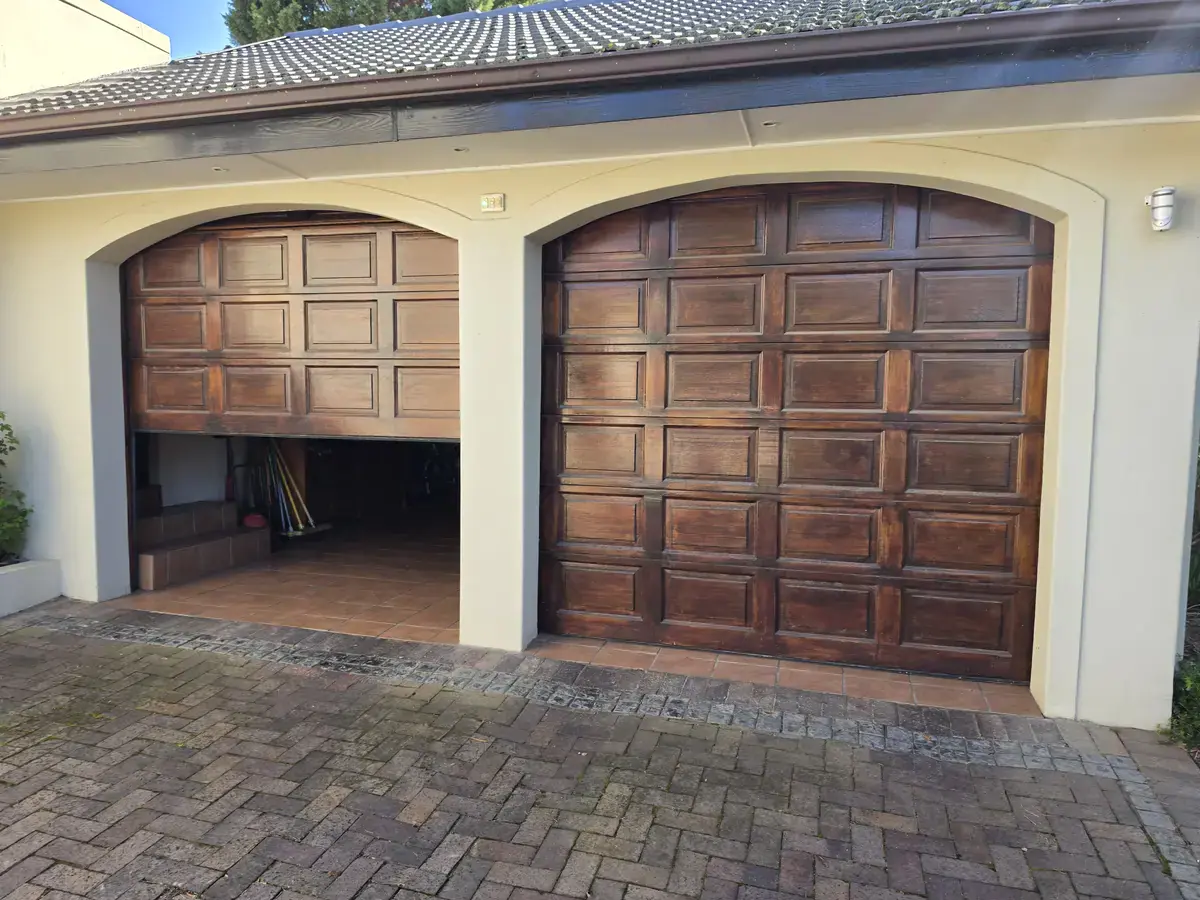 Eversdal home before exterior painting, showing weathered timber garage doors, pale walls and a tiled roof.